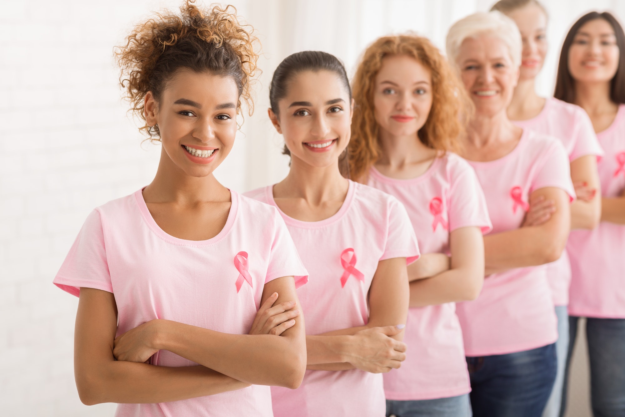 Female Volunteers In Breast Cancer T-Shirts Standing Over White Wall